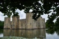 A ruined English medieval castle Bodiam Castle, UK reflected in a moat, seen through trees Royalty Free Stock Photo