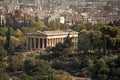 Ruins of ancient Greek temple surrounded by park or forest. Old building with columns with modern city, urban background