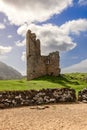 The ruins of Ardvreck Castle, set in the Scottish Highlands, rise above a stone wall, framed by a picturesque sky