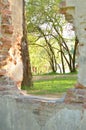 Ruins of brick stone old wall with window.Wall in the park with passage and green trees in the background.