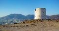 Ruins of broken windmill on a hill overlooking a city surrounded by mountains. Crumbling walls of abandoned lighthouse