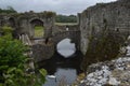 Ruins of an old castle on a moat with mossy old brick walls and overgrown bushes around them