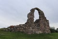 The ruins of an old stone wall against the background of a gloomy dark sky and green grass Royalty Free Stock Photo