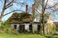 Ruins of small old abandoned suburban family house with destroyed roof partially covered with moss and broken windows