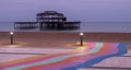 The ruins of West Pier, Brighton, East Sussex, UK. In the foreground, pebble beach and pavement painted in rainbow stripes.