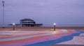 The ruins of West Pier, Brighton, East Sussex, UK. In the foreground, pebble beach and pavement painted in rainbow stripes.