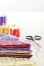 Ruler, cutting mat, stack of multi-colored pieces of fabric, pincushion, spools of thread, scissors, needle and thread