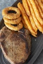 Rump steak dinner, with sweet potato fries and onion rings, on a black oval plate. Royalty Free Stock Photo