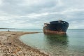 Run aground dry cargo ship. Abandoned rusty shipwrecked vessel. A man sits against the ship. Clear sea water and cloudy