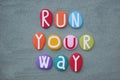 Run your way, creative slogan composed with multi colored stone letters over green sand