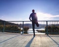 Runner doing stretching exercise on bridge. An active wiry man