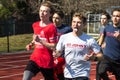 Runner gives hang loose sign with hands and sticks out his tongue while running in a group on a track