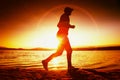 Runner in Sun rays on beach. Sportsman in baseball cap, jogging during the sunrise above sea Royalty Free Stock Photo