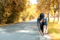 Running asian woman tying laces of running shoes before jogging through the road in the workout nature autumn park. Royalty Free Stock Photo