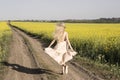 Running away blonde girl between yellow blooming fields.