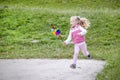 Running little blonde girl holding multicolored pinwheel.