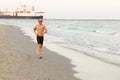 Runner training outside working at the beach. Fit young male sport fitness model exercising in full body in summer