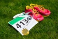 Running shoes, marathon race bib (number) and finisher medal on grass background,