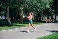 running smiling young sporty woman in park in sportswear on background of green trees on grey tiles in sunny windy Royalty Free Stock Photo