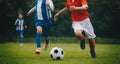 Running soccer players in duel. Youth athletes kicking black and white football ball