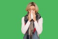 Runny nose, flu symptoms. Portrait of sick adult woman wrapped in warm scarf sneezing and blowing her nose in napkin Royalty Free Stock Photo