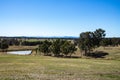 Rural Australian farmland with water dam, fences, hilltops, eucalyptus gum trees, blue sky