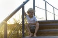 Rural boy in straw hat sitting outdoors at wooden stairs Royalty Free Stock Photo