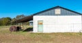 Rural building with colorful, rusty door in a grassy field, with overhang and rusty fluid tanks Royalty Free Stock Photo