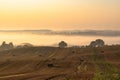 Rural colorful foggy landscape at sunrise. Harvested agricultural hilly wheat field with straw bales and foggy countryside dale Royalty Free Stock Photo