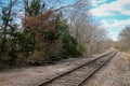 Rural country railroad train tracks leading through countryside with blue sky and green trees