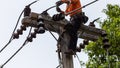 Rural electric poles are being repaired by electricians installing wires to connect. The tops of the electric poles are attached