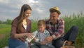 Rural family, happy woman pouring milk into glass to son and husband during picnic in nature in grain field