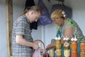 Rural food market. Man buying food from middle aged woman street seller, cans with pickles on a foreground. Klavdiivka