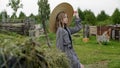 Rural girl in hat posing on haystack and hayfork background in countryside. Rustic teen girl on dry hayrick and