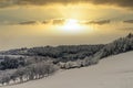 Idyllic bright winter countryside scene with a golden Sun breaking through the clouds over a snow field Royalty Free Stock Photo