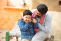 Rural Indian father and son putting coin into clay money box. Happy beard man and boy holding traditional piggy bank or Gullak,