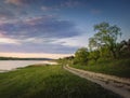 Rural landscape with a country road between lake and forest. Idyllic summer scene, peaceful evening with colorful sunset sky Royalty Free Stock Photo
