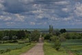 Rural landscape with a dirt road through a green field, beautiful cloudy sky Royalty Free Stock Photo