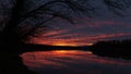 Rural landscape with dramatic light at sunset with red glow in clouds - tree silhouette and water reflection Royalty Free Stock Photo