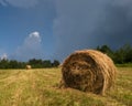 Rural landscape with hay stacks, field with roll bales, domestic livestock fodder, dark gloomy clouds