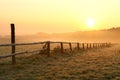 rural landscape at sunrise with wooden fence in the field in misty weather wooden fence in the field lit by rising sun in foggy Royalty Free Stock Photo