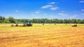 Rural landscape - tractor harvesting large round bales of straw in the field after harvest