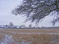 Scenic rural landscape of winter field and snowy branch with old village on background Royalty Free Stock Photo