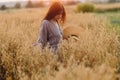 Rural life. Stylish woman with straw hat standing in oat field in sunset light. Atmospheric tranquil moment. Young female in Royalty Free Stock Photo