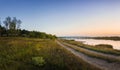 Rural panoramic landscape as a country road separates the lake from the forest. Beautiful evening scene, calm autumn background