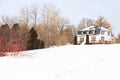 Rural patrimonial white house with metal sheet mansard roof seen in winter surrounded by bare trees and snowy land