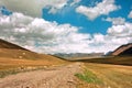 Rural road between beautiful colors mountains under white clouds sky Royalty Free Stock Photo