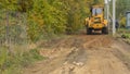 Rural road construction with grader in autumn daytime. The grader repairs the dirt road in the village.