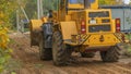 Rural road construction with grader in autumn daytime. The grader repairs the dirt road in the village.