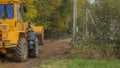 Rural road construction with grader in autumn daytime. The grader repairs the dirt road in the village